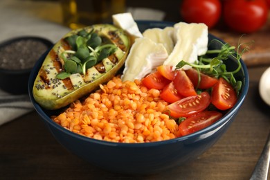 Photo of Delicious lentil bowl with soft cheese, avocado and tomatoes on wooden table