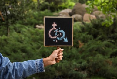 Photo of Woman holding chalkboard with gender symbols outdoors, closeup