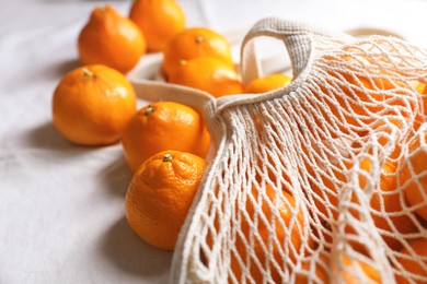 Photo of Net bag with many fresh ripe tangerines on white cloth, closeup