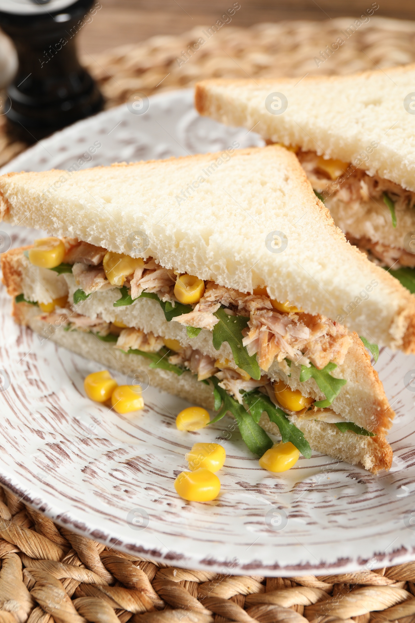 Photo of Delicious sandwiches with tuna, corn and greens on wicker mat, closeup