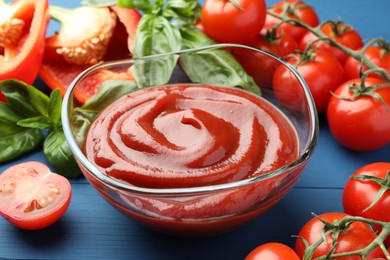 Photo of Bowl of tasty ketchup and ingredients on blue wooden table, closeup