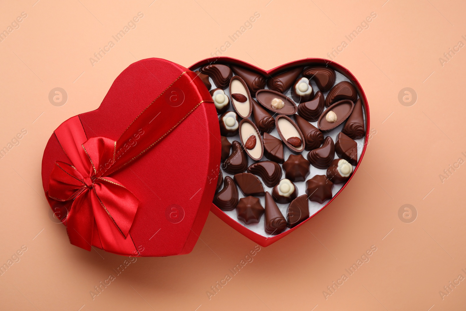 Photo of Heart shaped box with delicious chocolate candies on beige background, top view