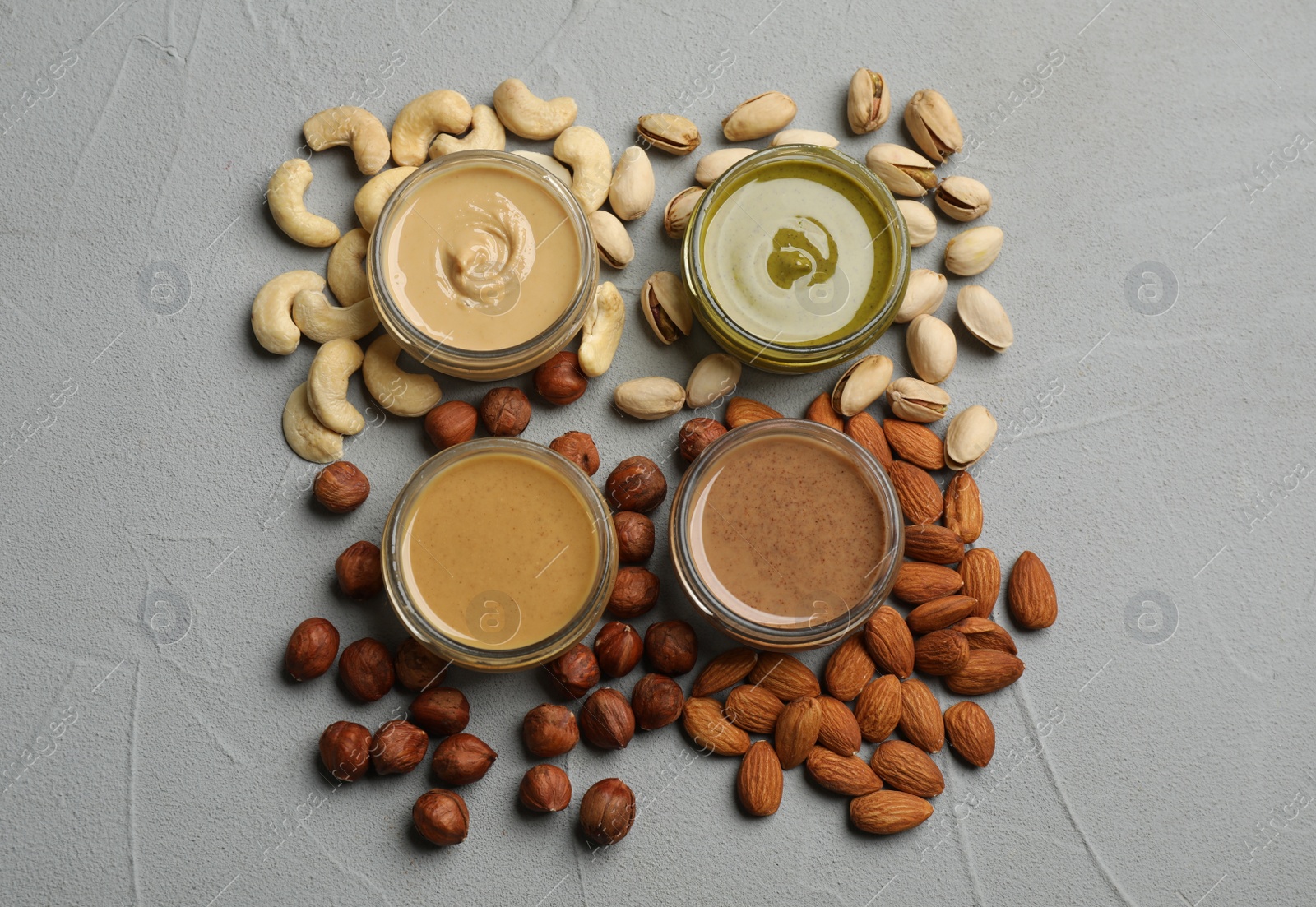 Photo of Jars with butters made of different nuts and ingredients on grey table, flat lay