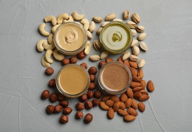 Jars with butters made of different nuts and ingredients on grey table, flat lay