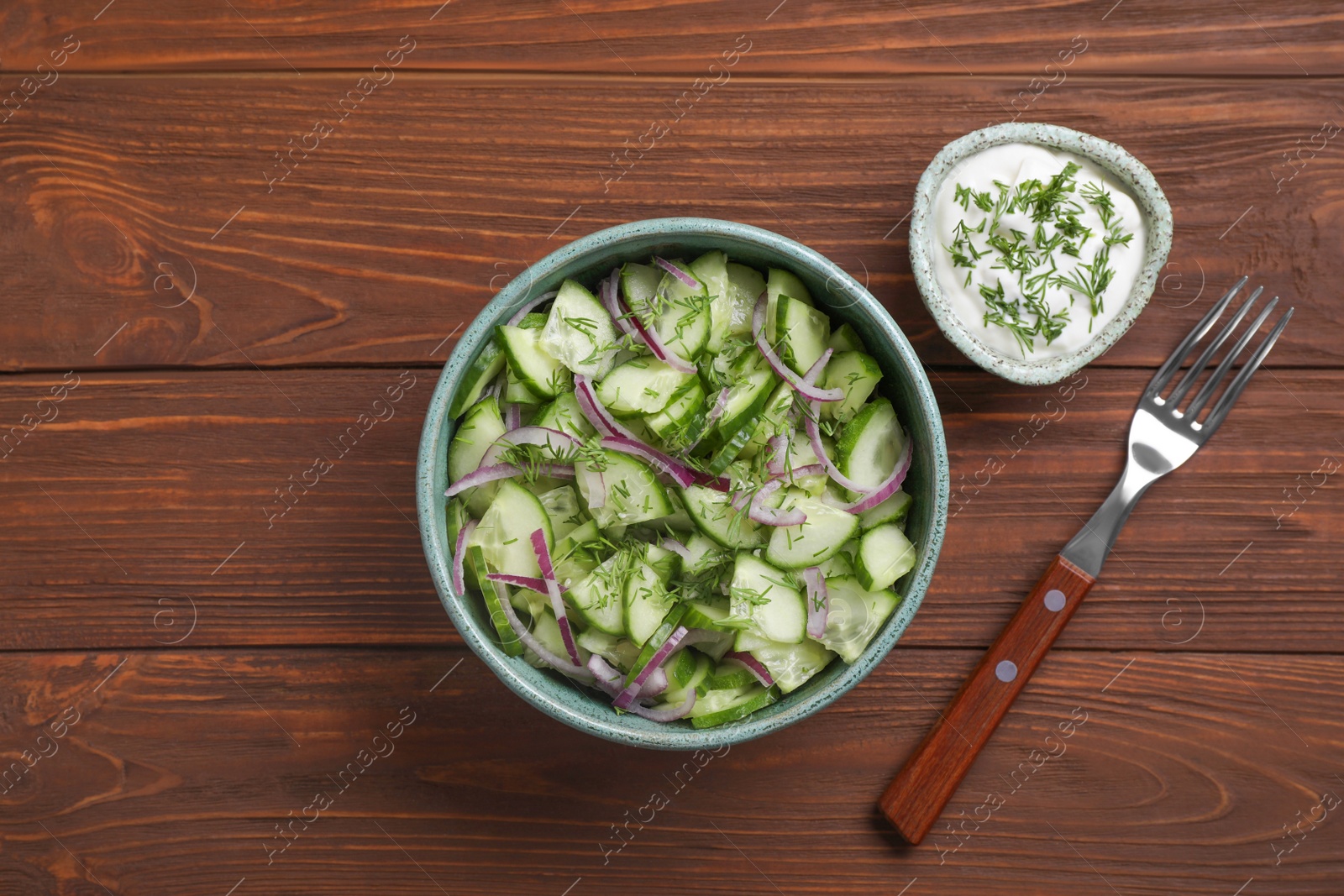 Photo of Flat lay composition with delicious fresh cucumber onion salad in bowl served on wooden table