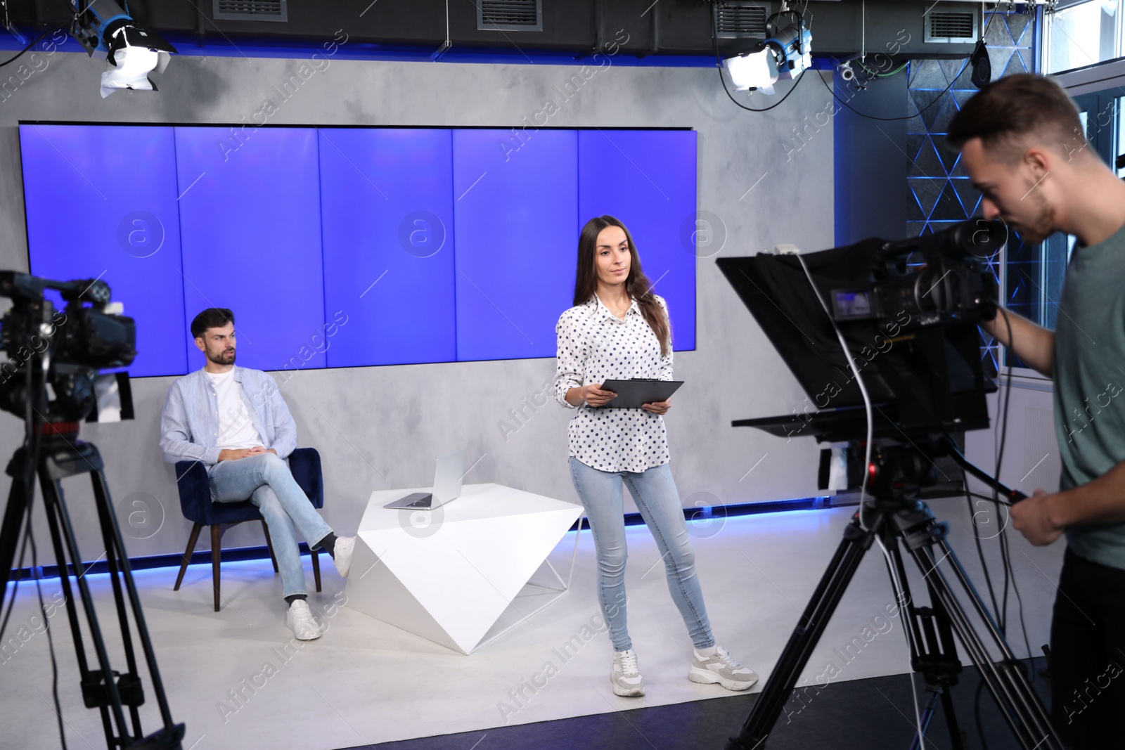 Photo of Presenters and video camera operator working in studio. News broadcasting