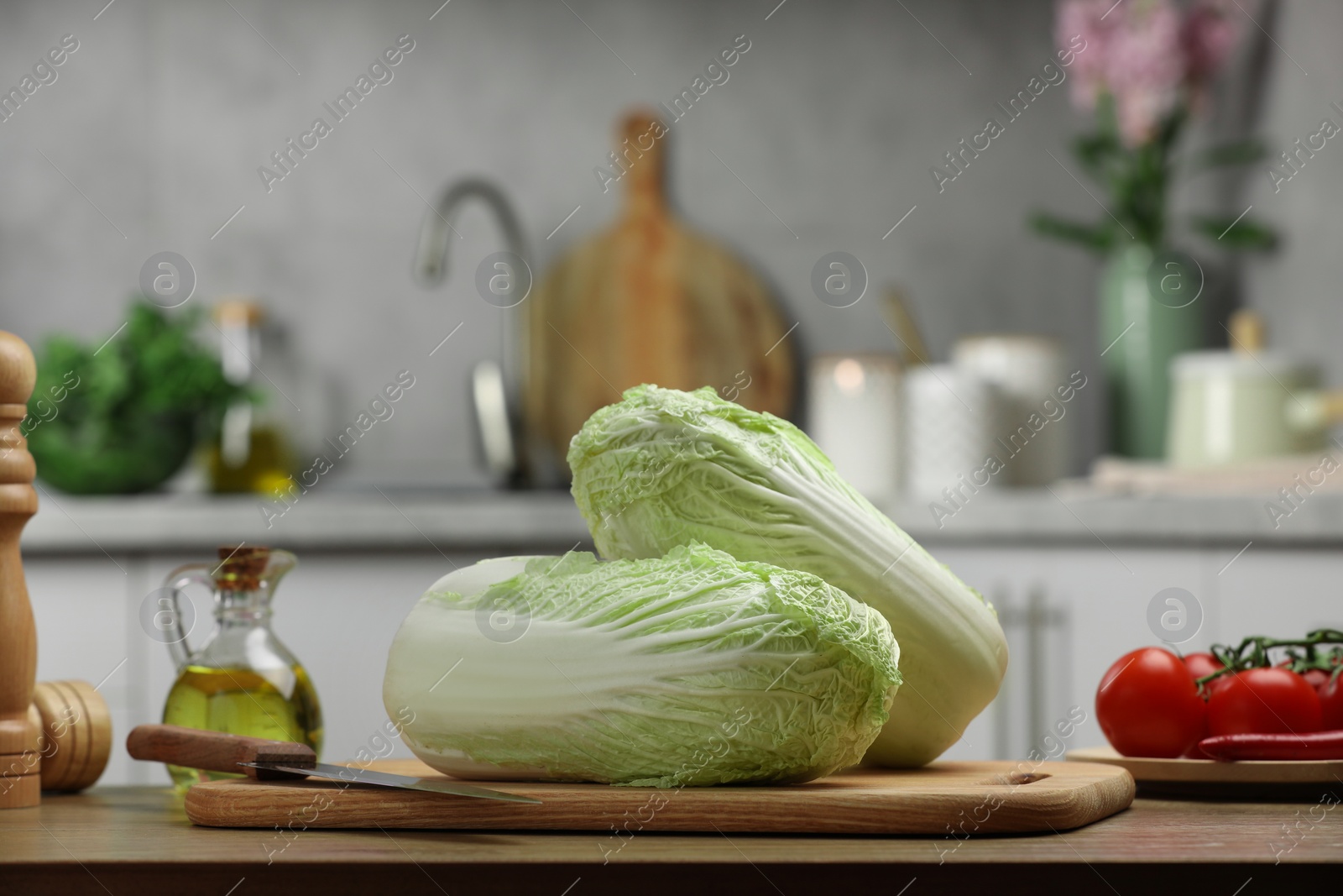 Photo of Fresh Chinese cabbages, knife, tomatoes and oil on wooden table in kitchen