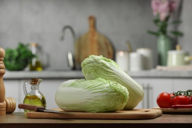 Fresh Chinese cabbages, knife, tomatoes and oil on wooden table in kitchen