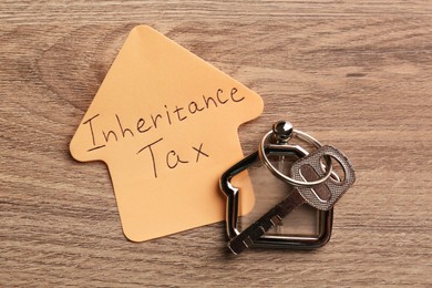 Photo of Inheritance Tax. Sticky note and key with key chain in shape of house on wooden table, flat lay