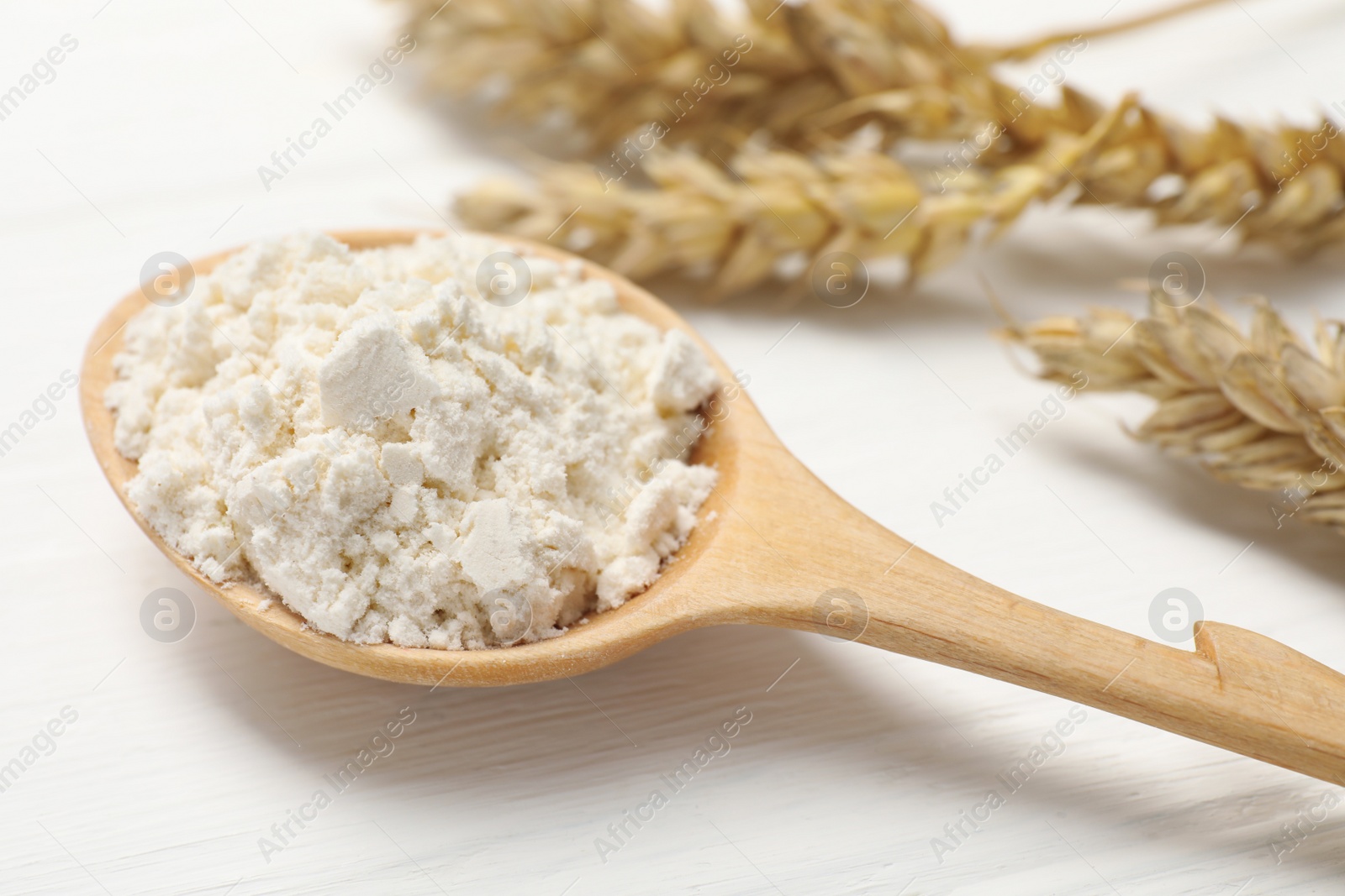 Photo of Spoon of wheat flour on white wooden table, closeup