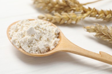 Spoon of wheat flour on white wooden table, closeup