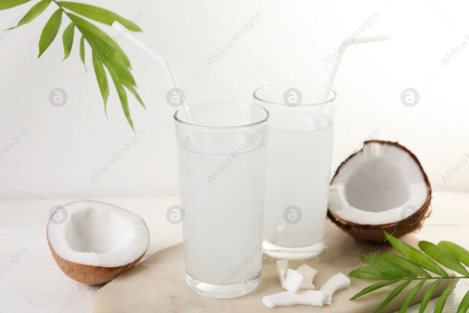 Photo of Glasses of coconut water, palm leaves and nuts on white table