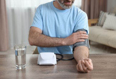 Photo of Man measuring blood pressure at table indoors, closeup