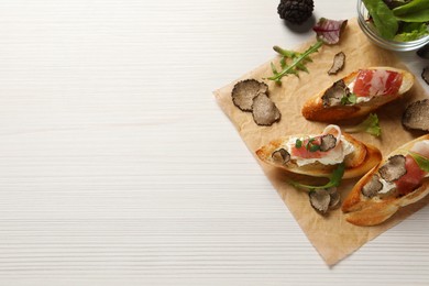 Photo of Delicious bruschettas with cheese, prosciutto and slices of black truffle on white wooden table, flat lay. Space for text