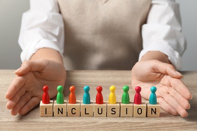 Photo of Woman protecting colorful pawns and wooden cubes with word Inclusion at table, closeup