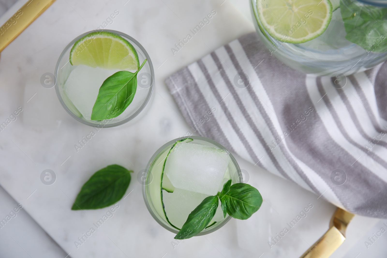 Photo of Tasty fresh cucumber water with sliced lime and basil on white marble table, flat lay