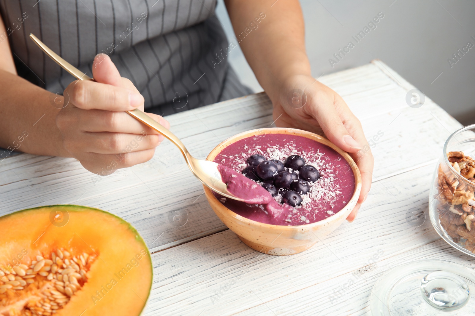 Photo of Woman eating tasty acai smoothie at table, closeup