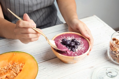 Woman eating tasty acai smoothie at table, closeup