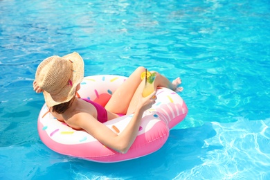 Young woman with cocktail in pool on sunny day