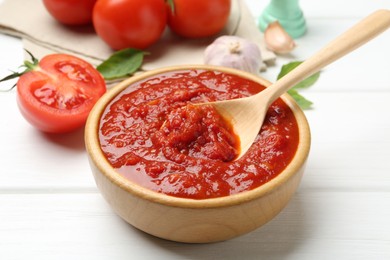 Photo of Homemade tomato sauce and spoon in bowl on white wooden table, closeup