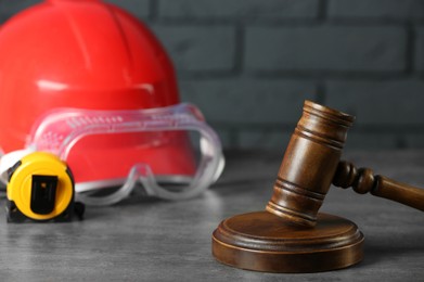 Photo of Construction and land law concepts. Gavel, hard hat, protective goggles and measuring tape on gray table, closeup
