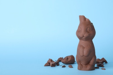 Photo of Broken chocolate Easter bunny on light blue background. Space for text