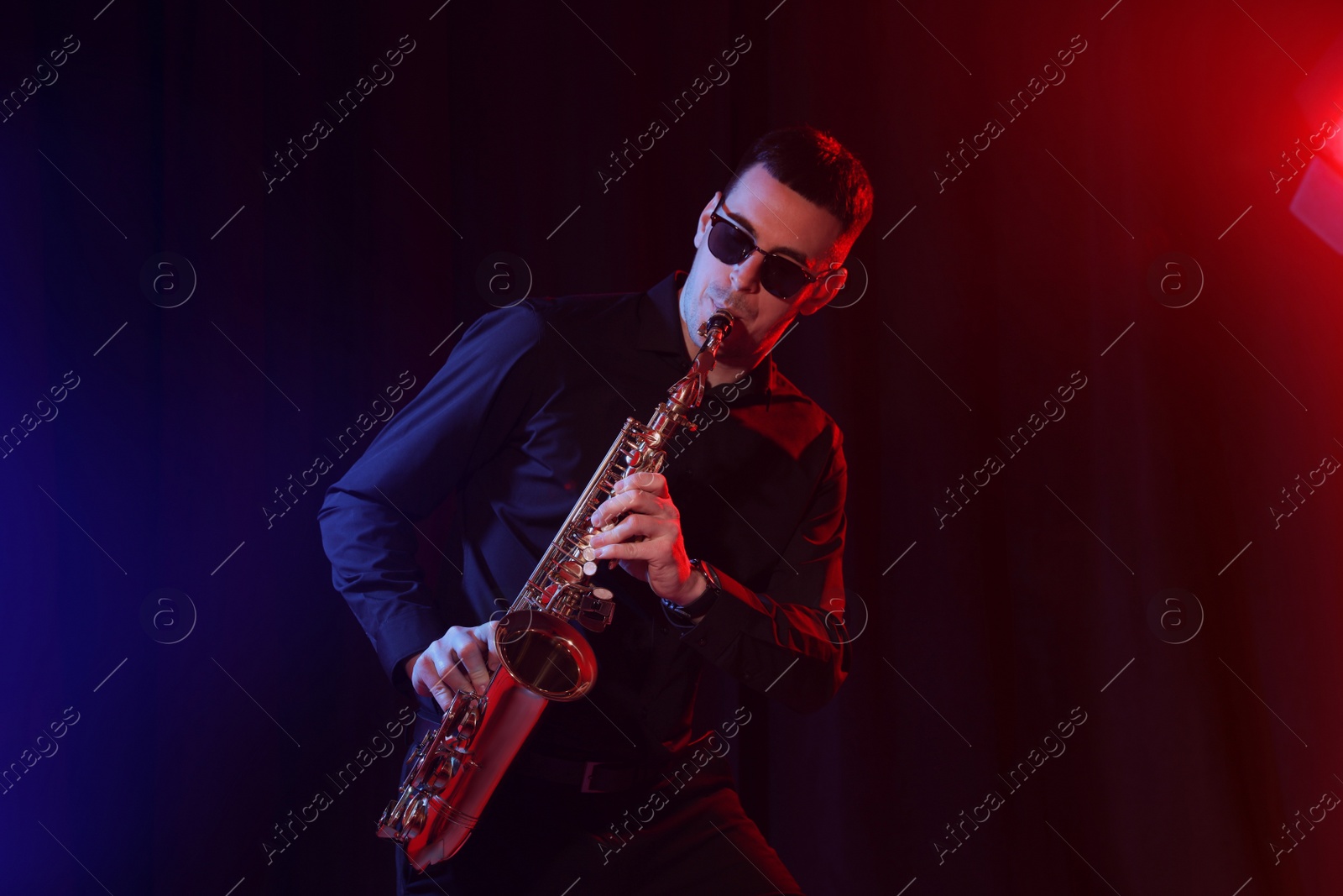 Photo of Young man playing saxophone on dark background