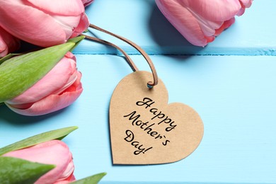 Image of Happy Mother's Day. Heart shaped greeting label and beautiful tulip flowers on light blue wooden table