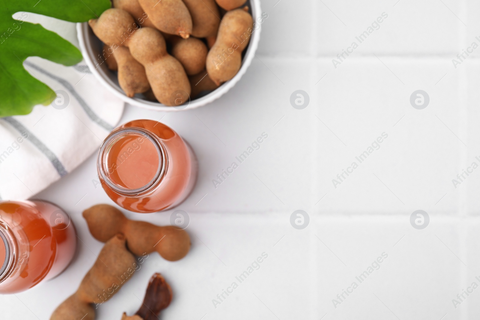 Photo of Tamarind juice and fresh fruits on white tiled table, flat lay with space for text