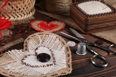 Heart shaped pieces of burlap fabric with different stitches and sewing tools on wooden table, closeup