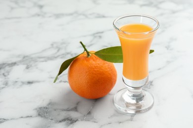Photo of Delicious tangerine liqueur in shot glass and fresh fruit on white marble table, closeup. Space for text