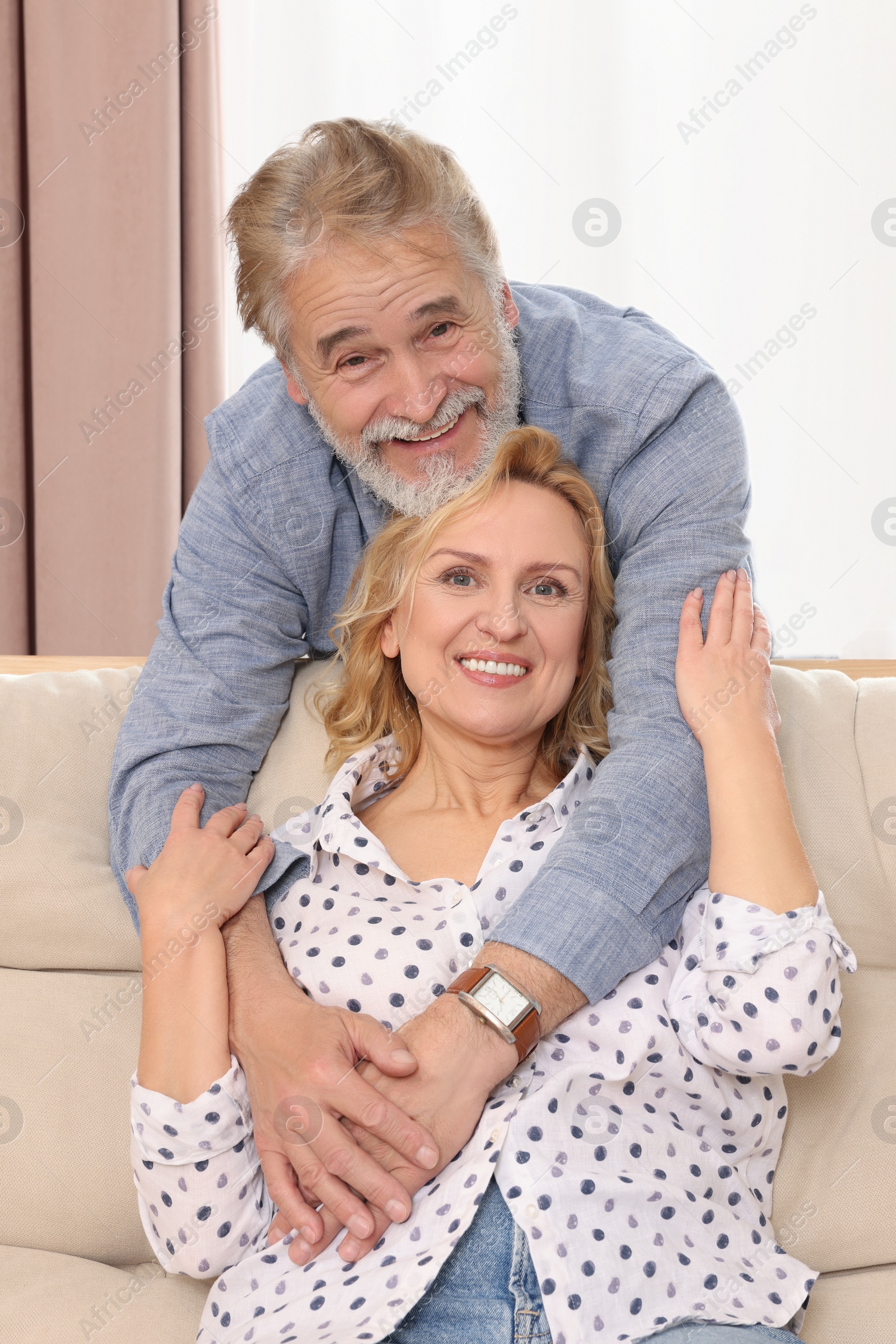 Photo of Happy mature couple hugging on sofa at home. Dating agency