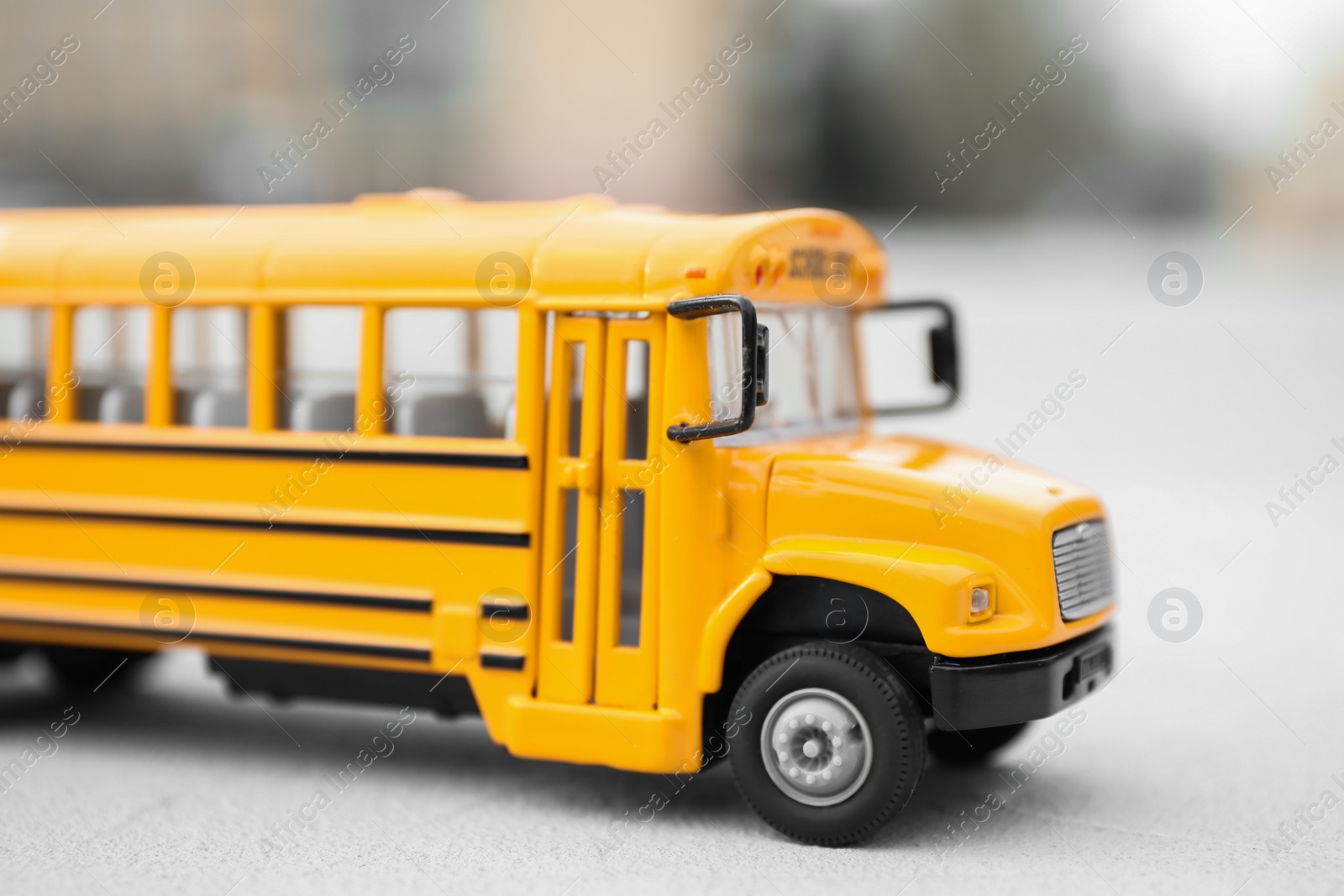 Photo of Yellow toy school bus against blurred background, closeup. Transport for students