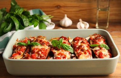 Photo of Baked eggplant with tomatoes, cheese and basil in dishware on wooden table
