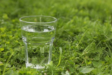 Photo of Glass of fresh water on green grass outdoors, closeup. Space for text