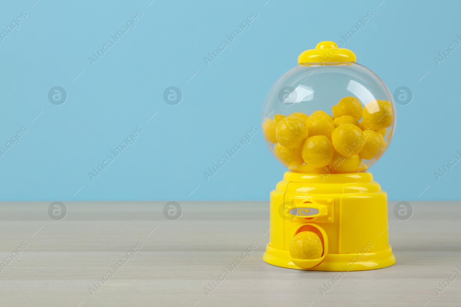 Photo of Small candy machine with lemon chewing gums on wooden table, space for text