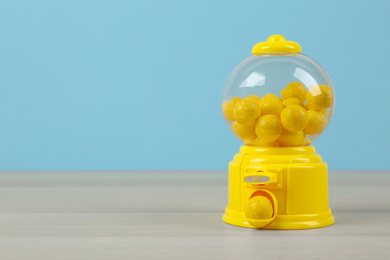 Photo of Small candy machine with lemon chewing gums on wooden table, space for text