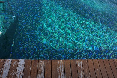 Photo of Clear rippled water in swimming pool and wooden deck outdoors, top view. Space for text