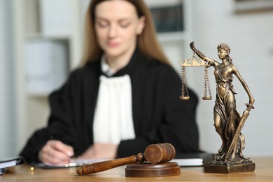 Photo of Judge working with document indoors, selective focus. Figure of Lady Justice and mallet on wooden table, closeup