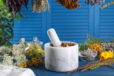 Photo of Mortar with pestle and many different herbs on blue wooden table
