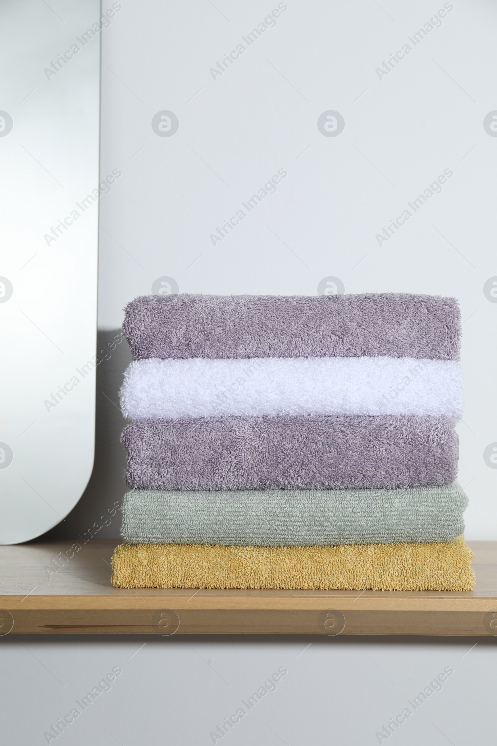 Photo of Stacked terry towels on wooden shelf near white wall