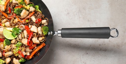 Photo of Stir-fry. Tasty noodles with meat and vegetables in wok on grey textured table, top view