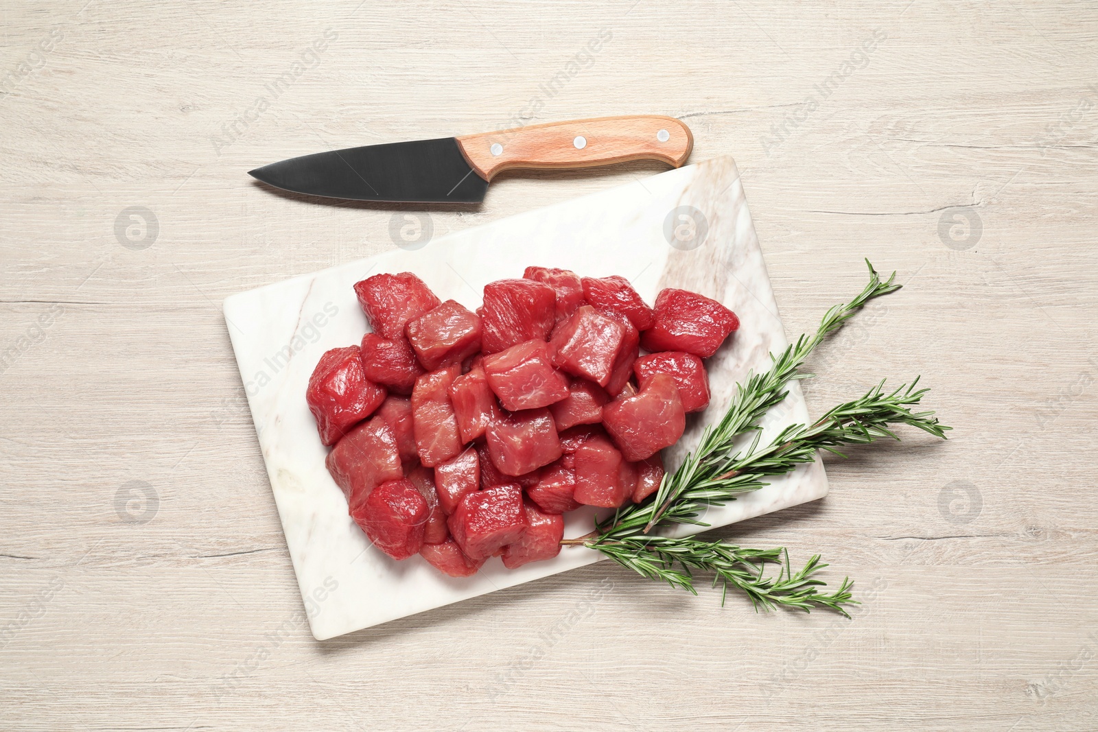 Photo of Cooking delicious goulash. Raw beef meat, rosemary and knife on white wooden table, flat lay