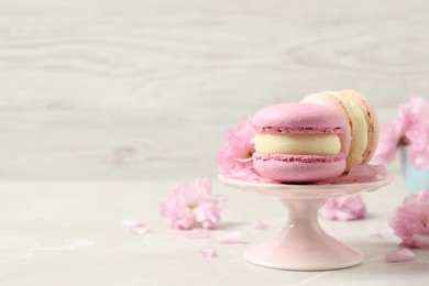 Photo of Delicious colorful macarons and pink flowers on light grey table, space for text