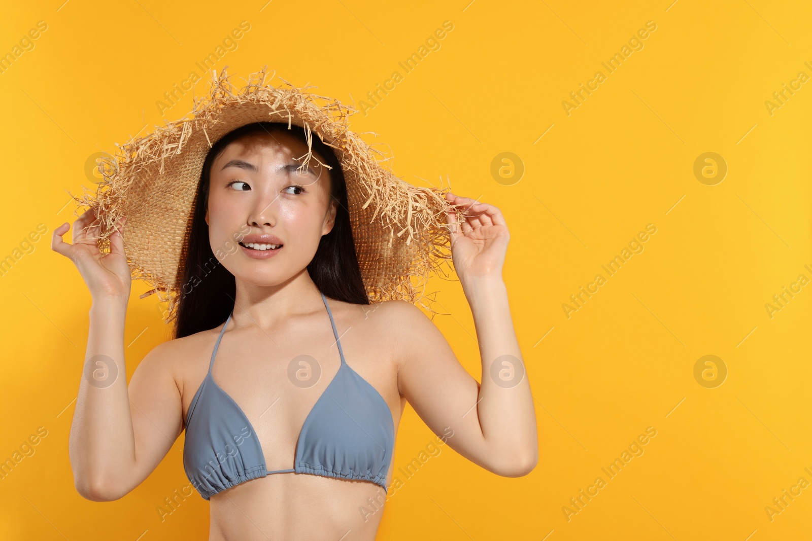 Photo of Beautiful young woman in straw hat on orange background, space for text