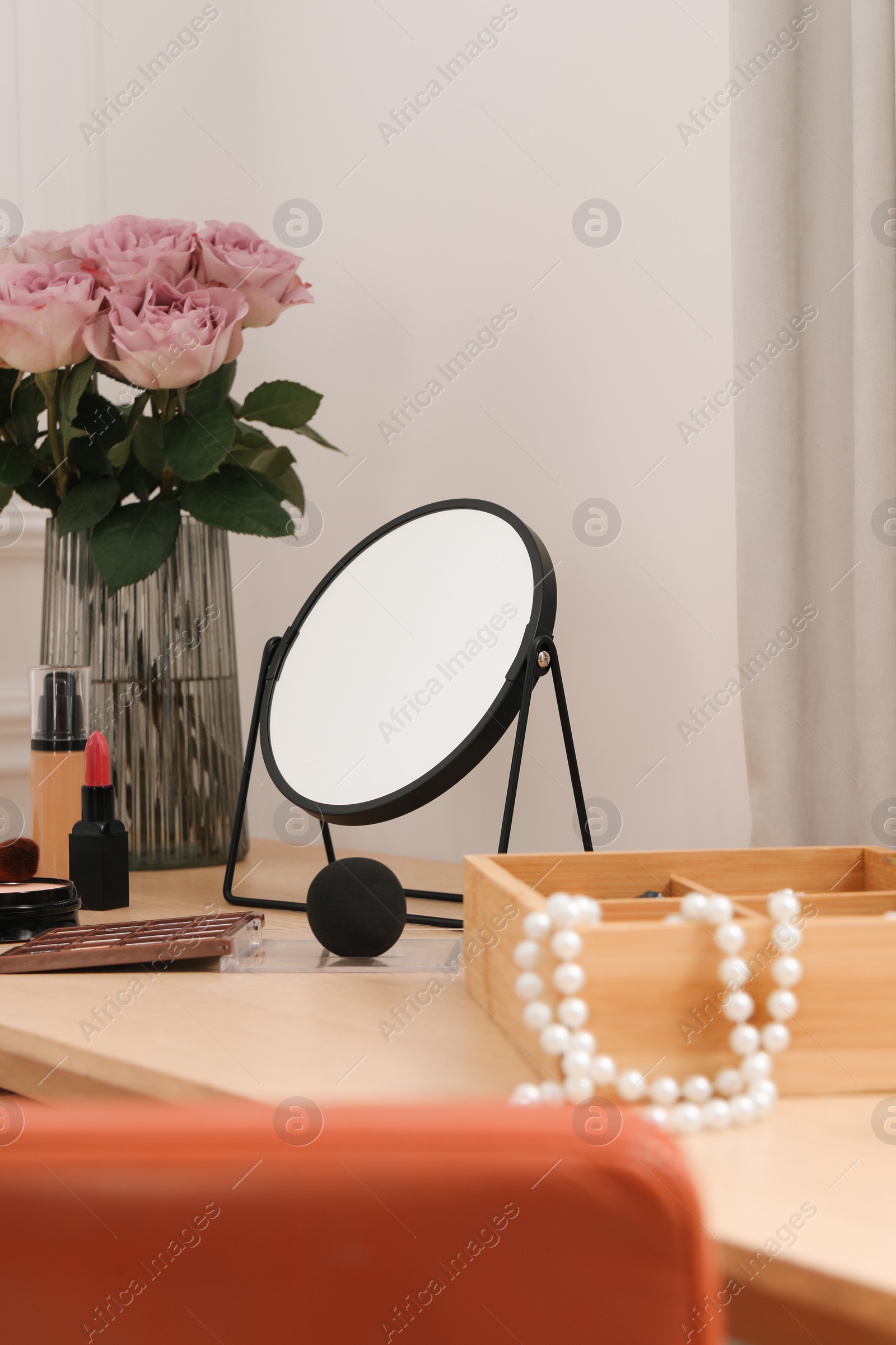 Photo of Mirror, cosmetic products, box of jewelry and vase with pink roses on wooden dressing table in makeup room