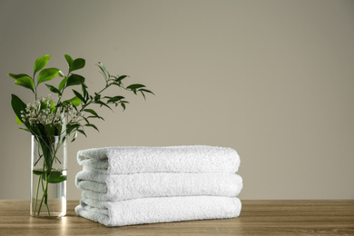 Photo of Clean bath towels and vase with green plants on wooden table. Space for text
