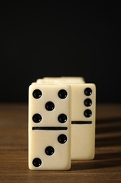 Photo of Domino tiles on wooden table against black background, closeup. Space for text