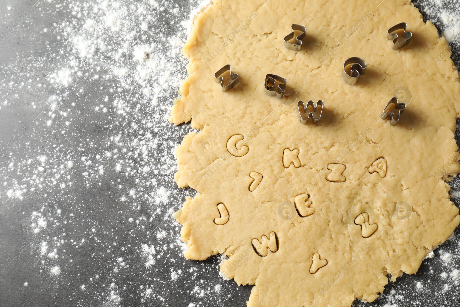 Photo of Making shortcrust pastry. Raw dough and cookie cutters on grey table, top view. Space for text