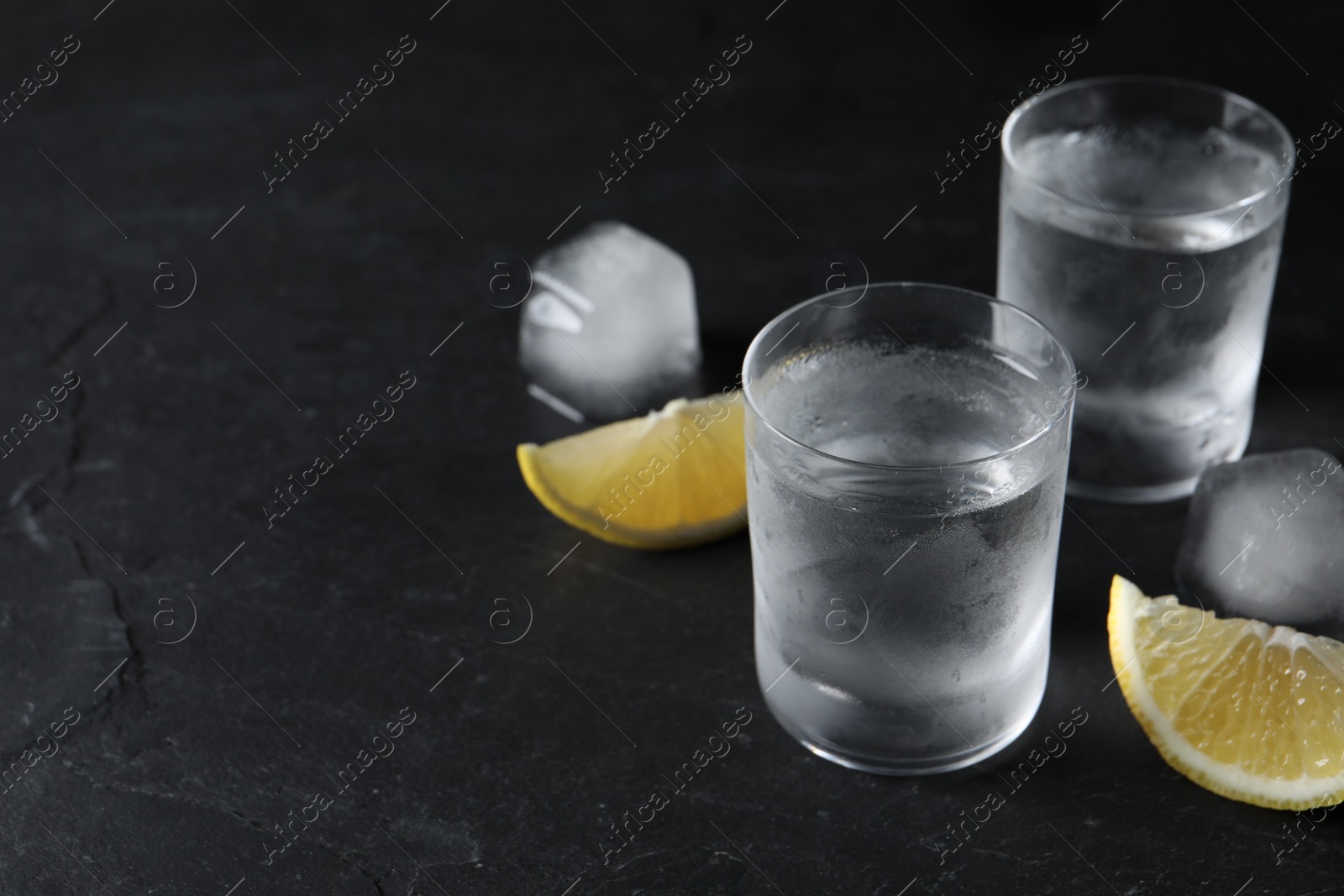 Photo of Shot glasses of vodka with lemon slices and ice on black background. Space for text